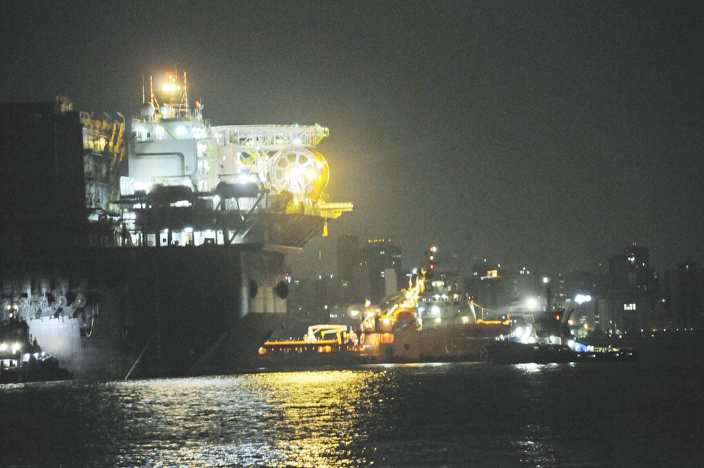 Embarcação iluminada em operação noturna, com barcos de apoio ao lado